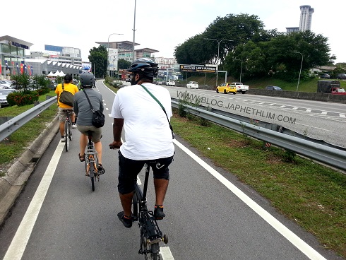 To the Left: A group of cyclist commuting on a dedicated bike lane along federal highway by keeping to the left lane to allow motorcyclist over take them. 